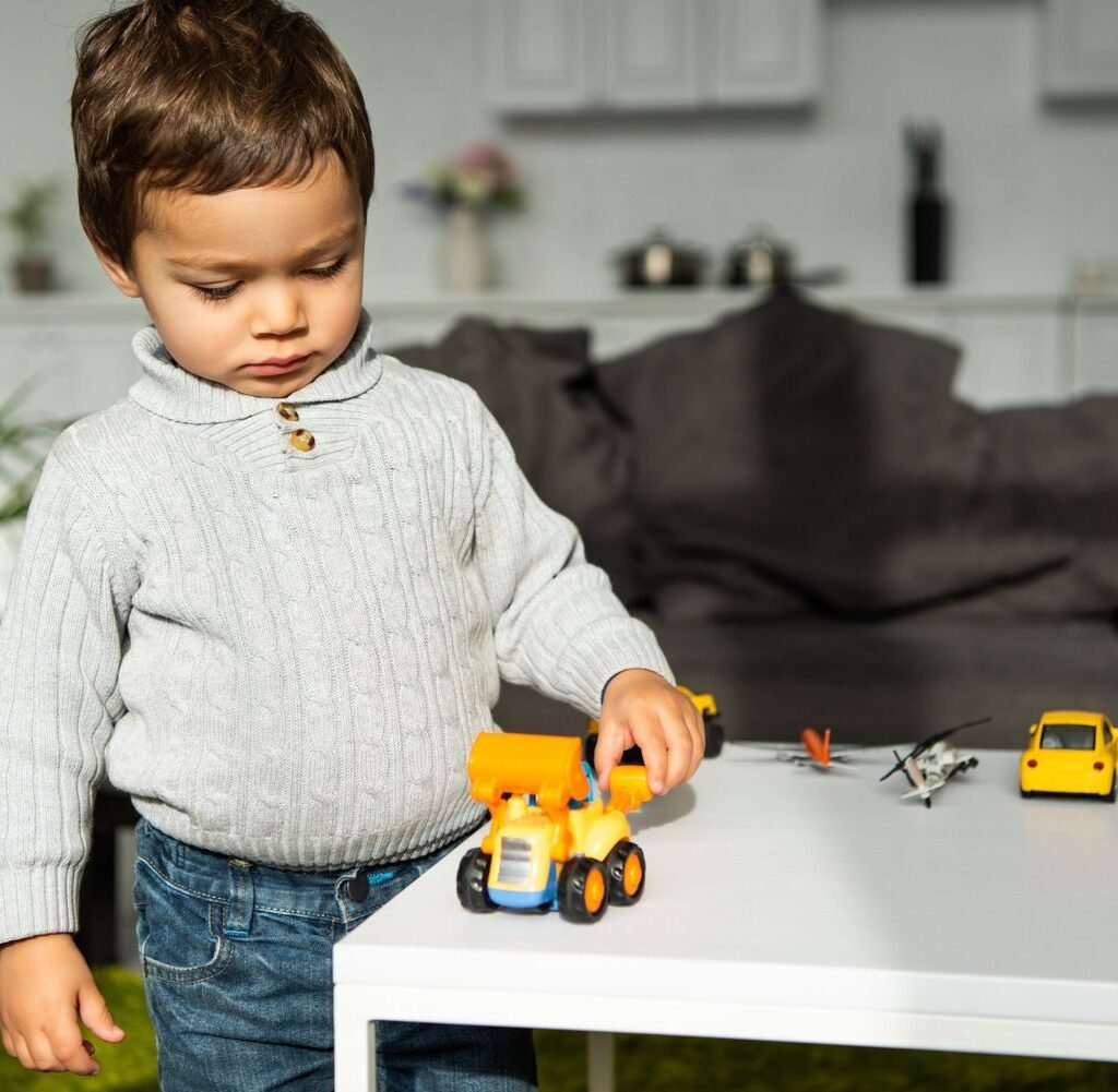 child playing with toy cars at table in living roo bn6q5np